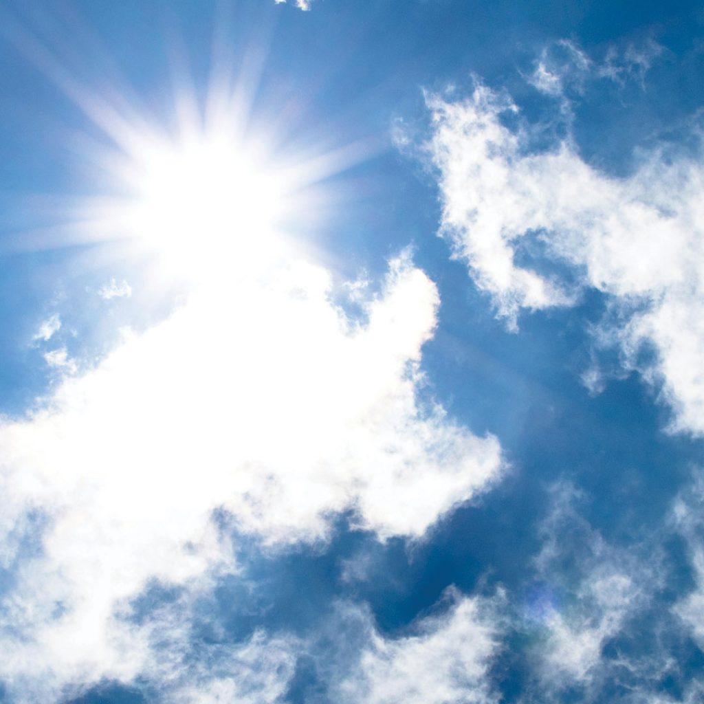 Sun peaking around white clouds in a blue sky